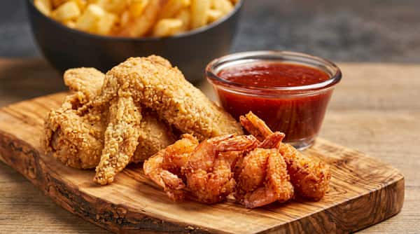 Fried chicken wings and shrimp with a small dish of red dipping sauce on a wooden board.