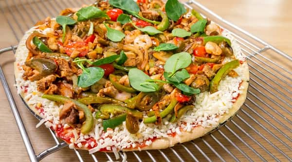Unbaked pizza with tomato sauce, mozzarella, peppers, onions, chicken, shrimp, cherry tomatoes, and spinach.