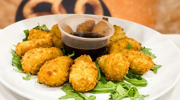 Fried zucchini fritters with a side of dark dipping sauce on a bed of arugula, with a restaurant logo.
