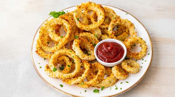 Crispy golden-brown onion rings with chopped parsley, served with a small bowl of ketchup.