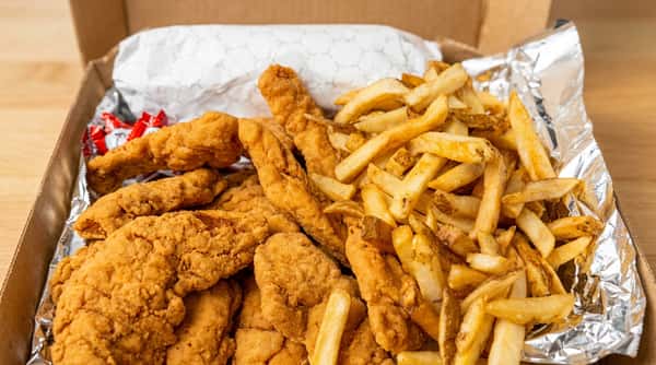 Fried chicken tenders and french fries in a foil-lined takeout box.
