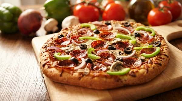Pepperoni pizza with green peppers, red onion, black olives, and mushrooms on a wooden cutting board.
