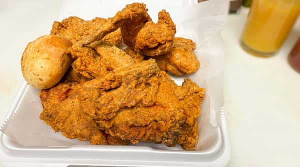 Fried chicken pieces and a bread roll in a white styrofoam container.