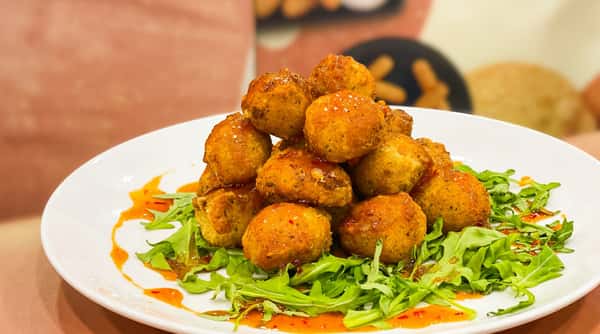 Golden-brown fried arancini balls drizzled with sauce on a bed of fresh arugula.