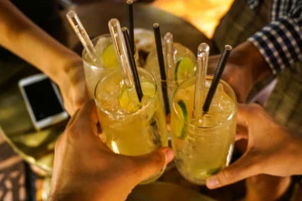 Four people clinking glasses of iced cocktails garnished with lime slices in a celebratory toast.