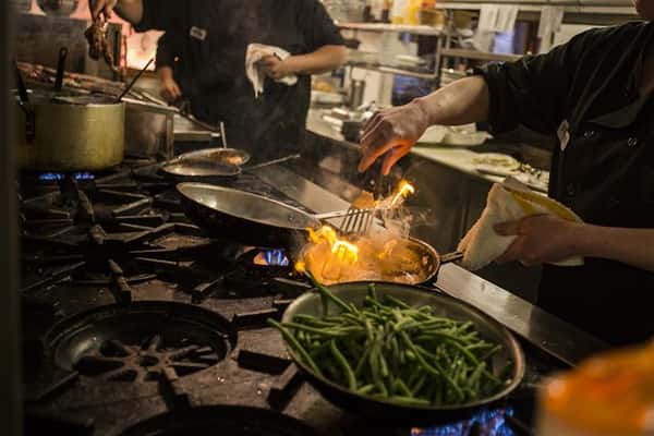 Two chefs in the kitchen in front of stove top cooking.
