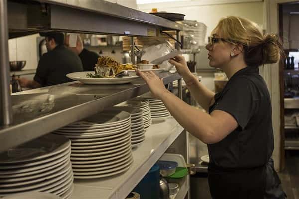 Woman in the kitchen grabbing plates to be served.