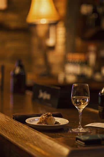 Plate of food and a glass of white wine on the bar top.