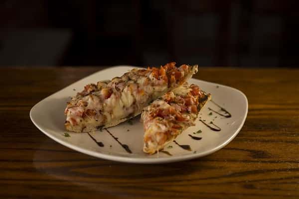Plate of two pieces of bruschetta, Grilled French baguette, topped with diced tomato, red onion, garlic, mozzarella cheese and a drizzle of balsamic glaze.