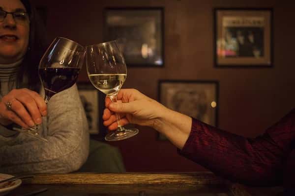 Two women clinking their wine glasses, one with red wine and one with white wine.
