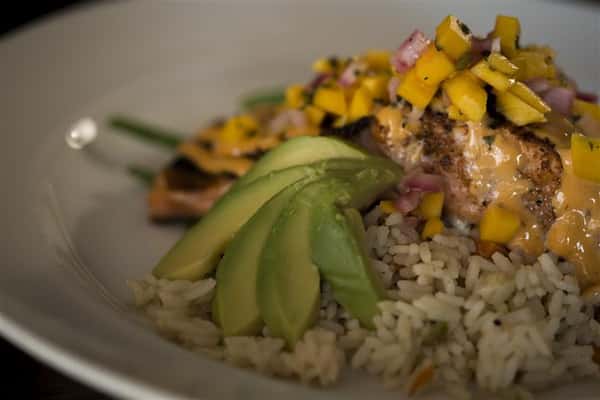 Close up of the Blackened Grilled Salmon topped with avocado, mango salsa and lemon chipotle aioli served with rice pilaf.
