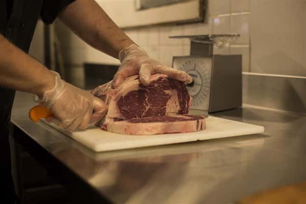 Chef cutting raw steak into pieces.