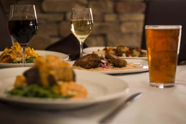 Four plates on the table with the focus on crab cakes all served with a pint of beer, a glass of white wine and a glass of red wine.