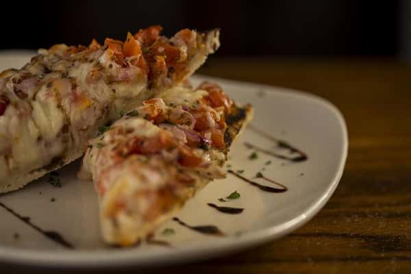 Plate of two pieces of bruschetta, Grilled French baguette, topped with diced tomato, red onion, garlic, mozzarella cheese and a drizzle of balsamic glaze.