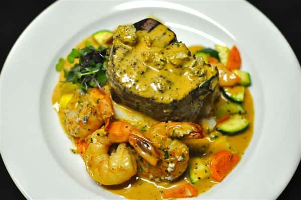 Steak and three shrimp topped with a creamy yellow sauce and served with mixed vegetables.