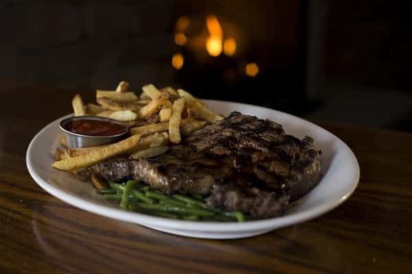 Grilled steak served with a side of green beans as well as french fries with a side of ketchup.