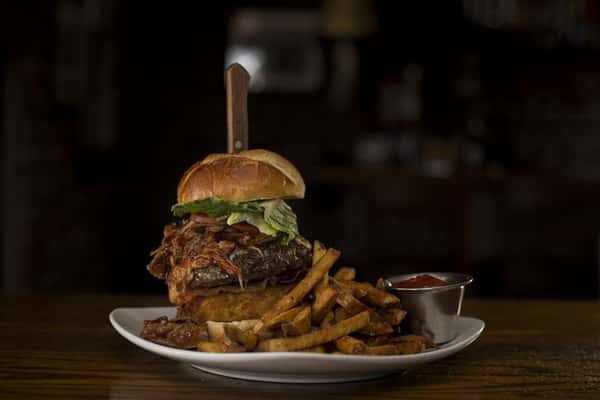 Cheese burger with a steak knife sticking in the top, topped with lettuce, tomato, caramelized onions and a side of french fries with ketchup.