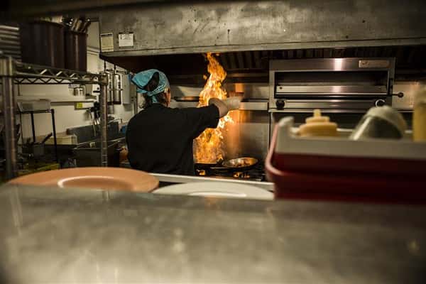 Chef in front of the stove top with flames.