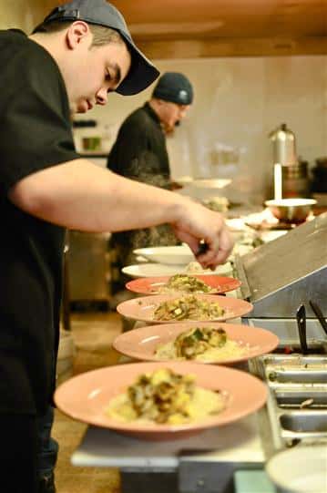 Chefs in the kitchen preparing a row of plates.