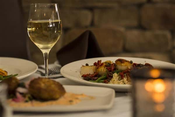 Three plates of food on the table with a glass of white wine.