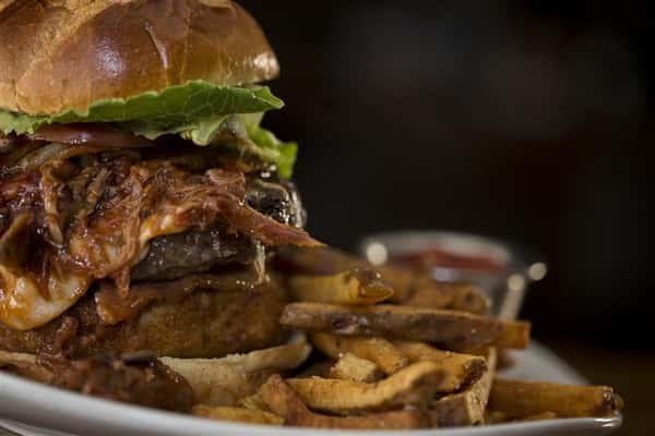 Close up of cheese burger with caramelized onions, lettuce, and tomato. Served with french fries and ketchup on the side.