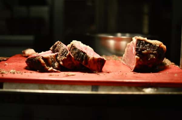 Pieces of cooked steak with a rare center being cut on a cutting board.