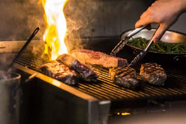 Five steaks on a grill with flames.