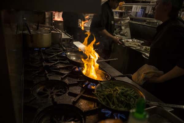 View of stove top with 3 pans, one with green beans and the other with flames.