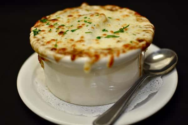 French Onion Soup in a bowl with melted cheese over top and a spoon on the side.