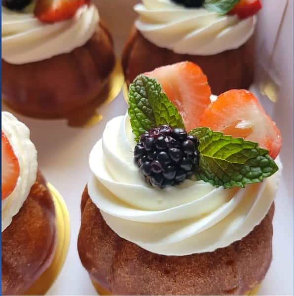 Mini bundt cakes topped with swirls of white frosting, strawberries, blackberries, and fresh mint leaves