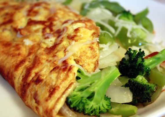 Cheese omelet stuffed with broccoli and sautéed onions, served with fresh greens on white plate