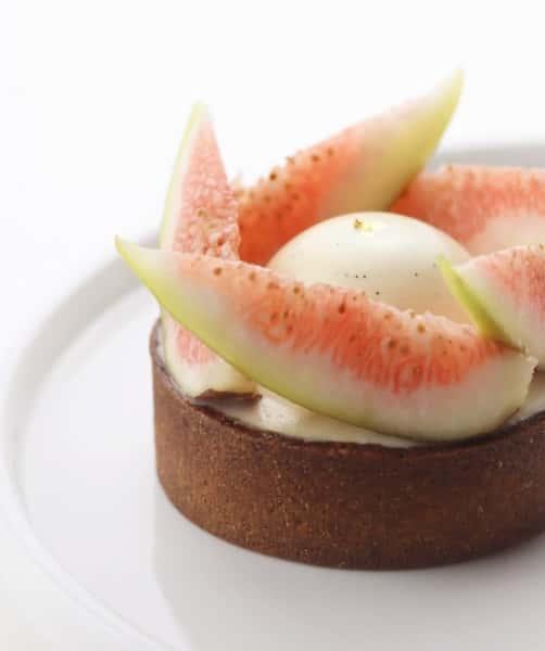 Fig tart with creamy filling, topped with fresh pink fig slices arranged around a smooth white dome