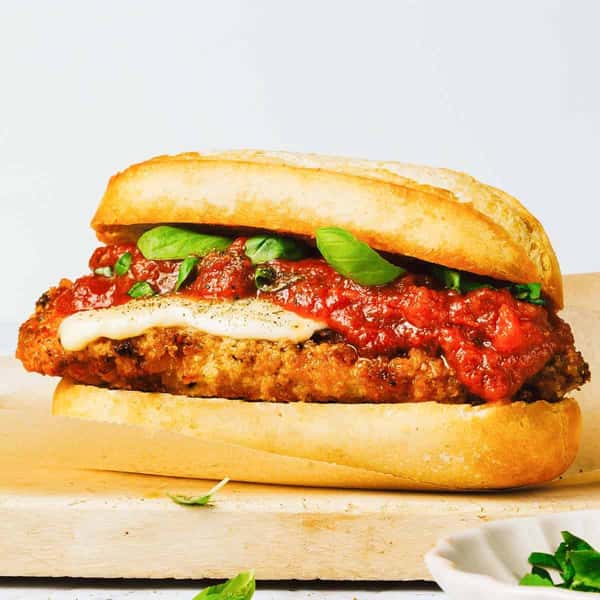 Chicken Parmesan sandwich on a toasted roll, featuring a crispy breaded chicken cutlet topped with melted mozzarella, rich marinara sauce, and fresh basil leaves.