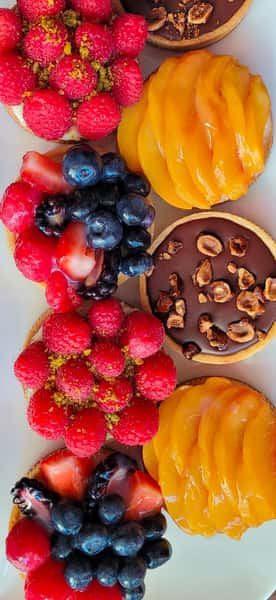 Assorted mini fruit tarts topped with raspberries, blueberries, strawberries, mango slices, and chocolate hazelnut glaze