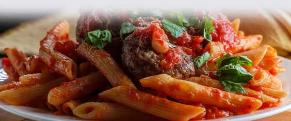 Penne pasta tossed in marinara sauce, topped with meatballs and fresh basil leaves.
