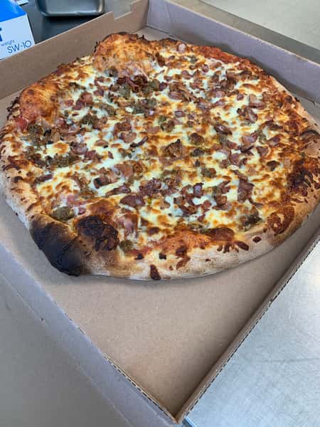 Large meat-topped pizza with melted cheese and a charred crust in an open cardboard box.