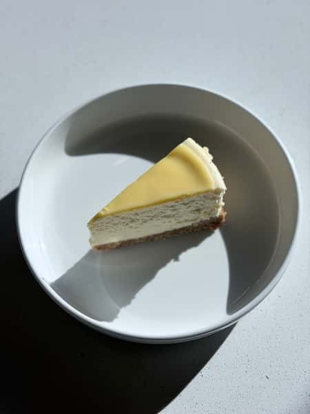 Slice of creamy cheesecake with smooth topping on a white plate in natural light