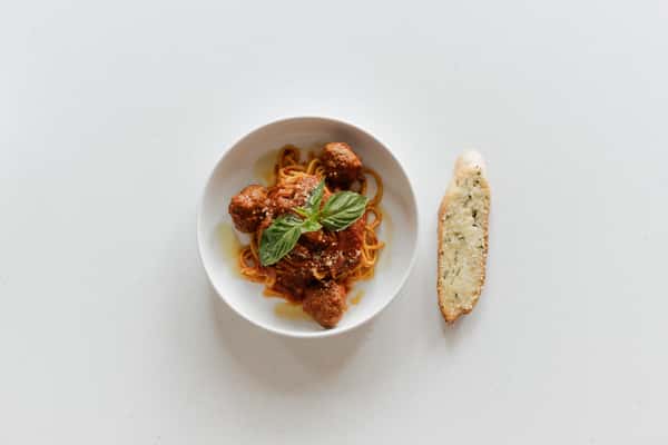 Spaghetti and meatballs in rich tomato sauce topped with fresh basil and grated cheese in a white bowl