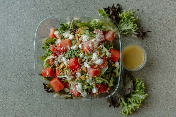 Fresh salad with watermelon, feta cheese, pistachios, and mixed greens served with dressing