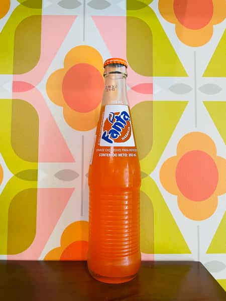 Fanta orange soda in glass bottle with vibrant retro patterned background