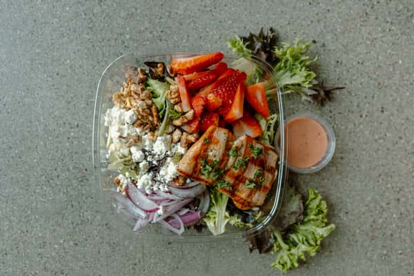 Grilled chicken salad with strawberries, walnuts, feta, red onions, and mixed greens served with dressing
