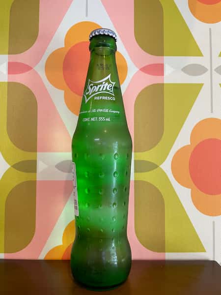Chilled Sprite glass bottle with condensation against retro patterned background