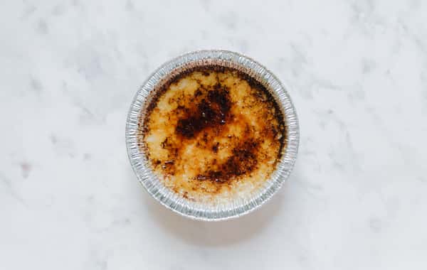 Crème brûlée dessert with caramelized sugar crust in a foil ramekin on a light surface