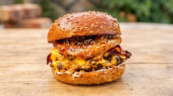 Burger with sesame seed bun, melted cheese, bacon, caramelized onions, and white sauce.