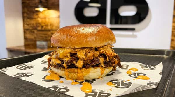 Double patty burger with melted cheese and orange sauce, on custom-wrapped paper on a black tray.