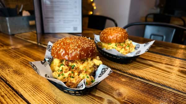 Two burgers topped with mac and cheese, fried onions, and chives, served on a wooden table.