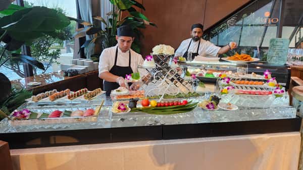 Two chefs preparing sushi behind an elaborate ice display filled with assorted rolls and nigiri.