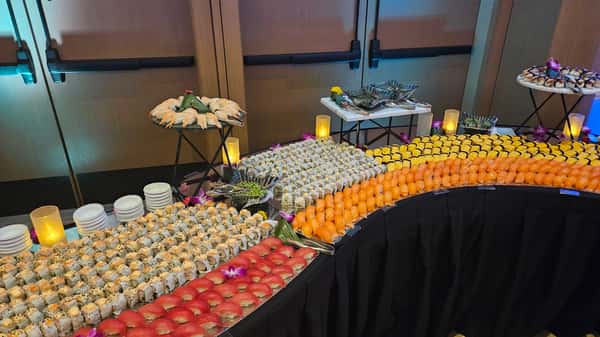 Large catered sushi buffet featuring rows of rolls, salmon and tuna nigiri, and shrimp platters.