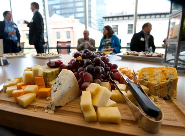 Cheese board with red grapes in the middles and people sitting at a table in the background