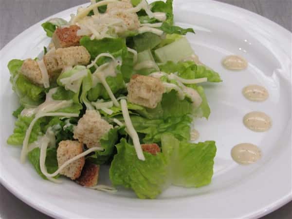 Caesar salad topped with shredded cheese and decorated with Caesar dressing